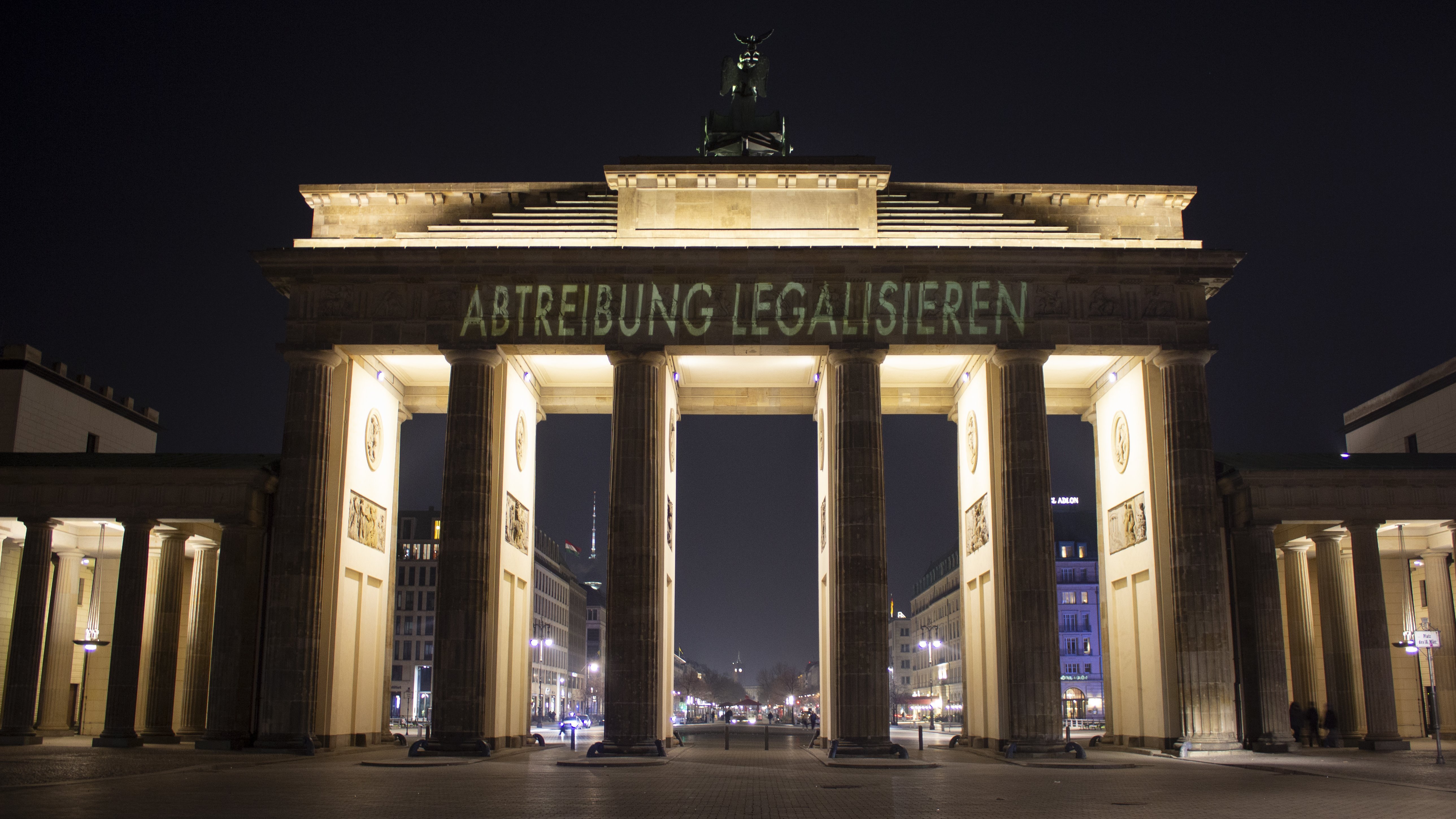 Auf dem Foto ist das Brandenburger Tor in Berlin bei Nacht zu sehen. Auf das Bauwerk wurde der Schriftzug "ABTREIBUNG LEGALISIEREN" projiziert. Die Beleuchtung des Tores hebt die Architektur hervor, während der dunkle Nachthimmel einen starken Kontrast zur Projektion bildet.