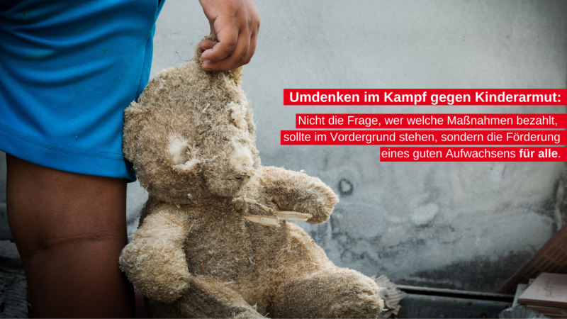 Das Foto zeigt eine Person in blauen Shorts, die neben einer Wand steht. Vor der Wand befindet sich ein großer Teddybär, dem die Gesichtszüge fehlen. An der Wand steht ein Text auf Deutsch: “Umdenken im Kampf gegen Kinderarmut: Nicht die Frage, wer welche Maßnahmen bezahlt, sollte im Vordergrund stehen, sondern die Förderung eines guten Aufwachsens für alle.”