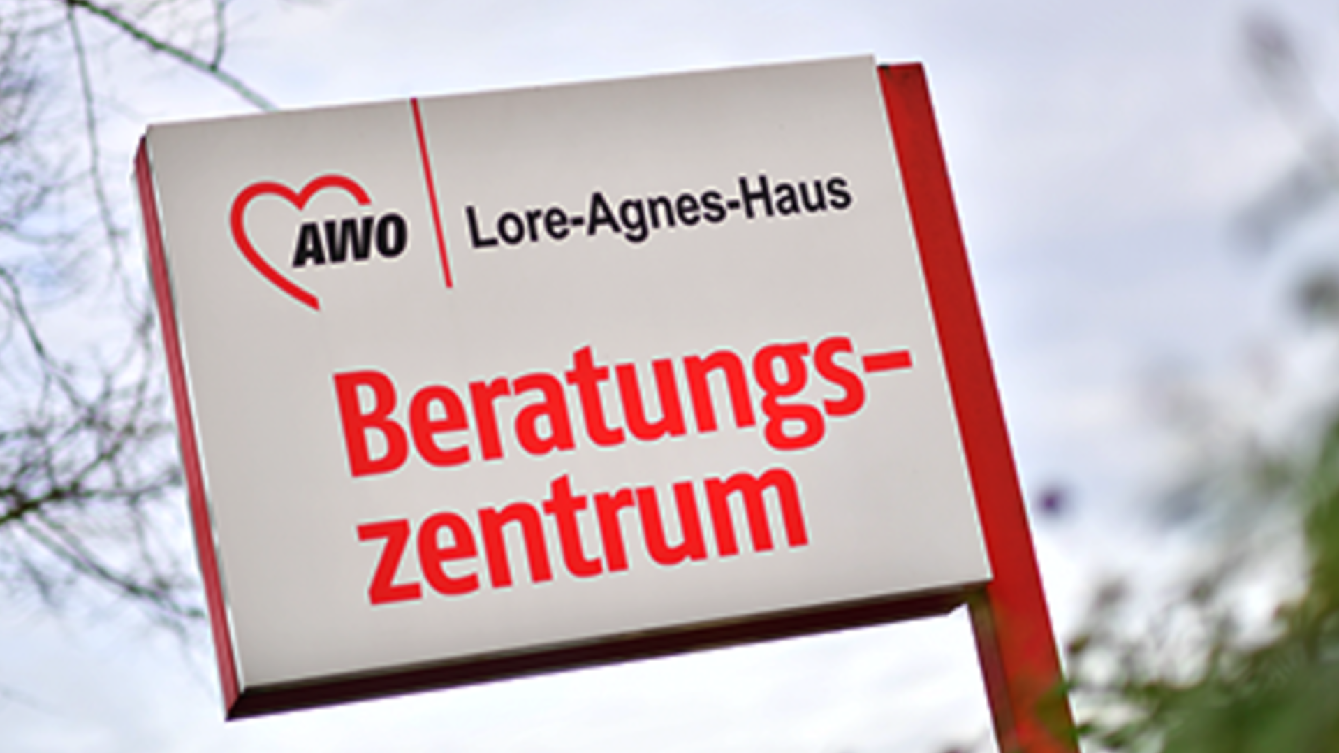 Das Foto zeigt das AWO Logo mit dem Zusatz "Lore-Agnes-Haus" und Beratungszentrum. Es handelt sich dabei um ein Hinweisschild an einer Straßenecke