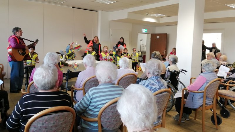 Das Bild zeigt singenden Kinder und Bewohner*innen die den Martinsliedern lauschen.