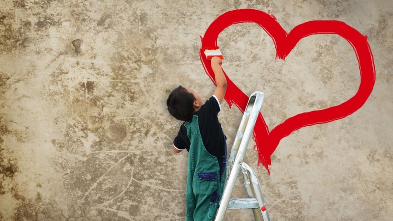 Das Foto zeigt einen Jungen auf einer Leiter, der mit roter Farbe die Umrisse eines Herzes mit roter Farbe an eine Wand malt