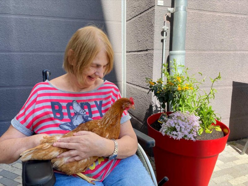 Das Foto zeigt eine Bewohnerin mit einem Huhn