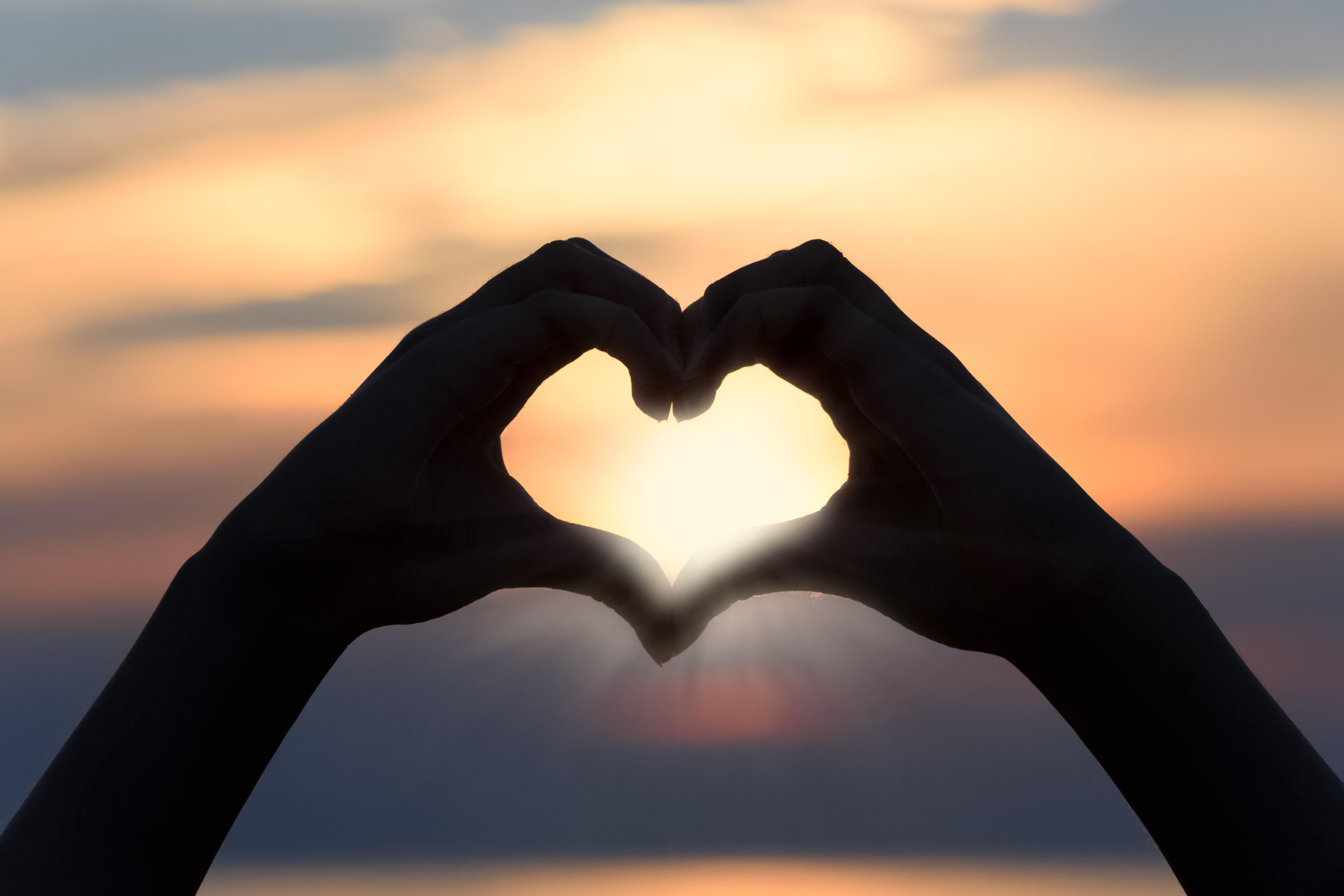 Das Foto zeigt ein aus Händen geformtes Herz vor einem Sonnenuntergang